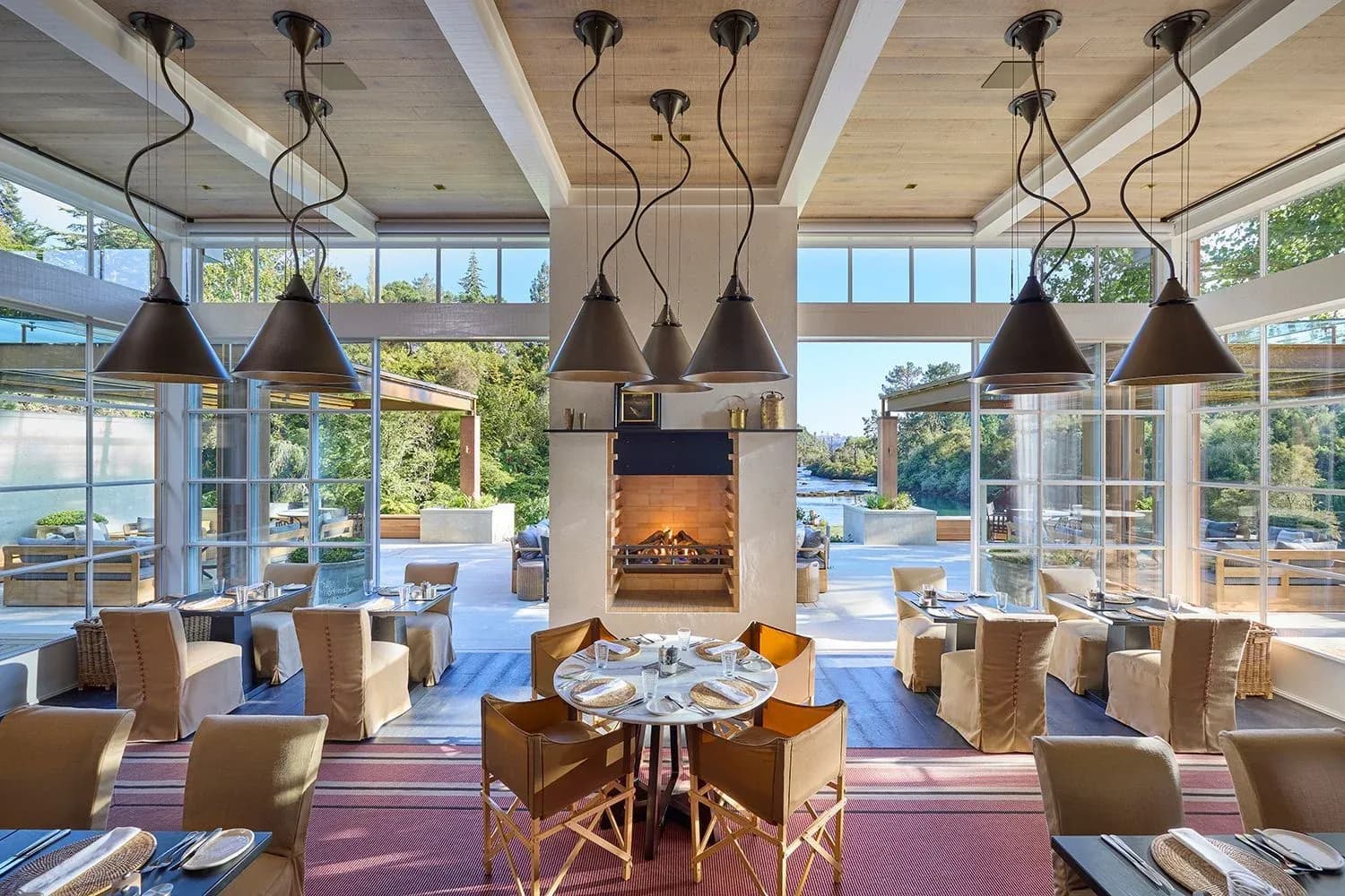 Dining area with large windows, a central fireplace, and tables set with place settings.