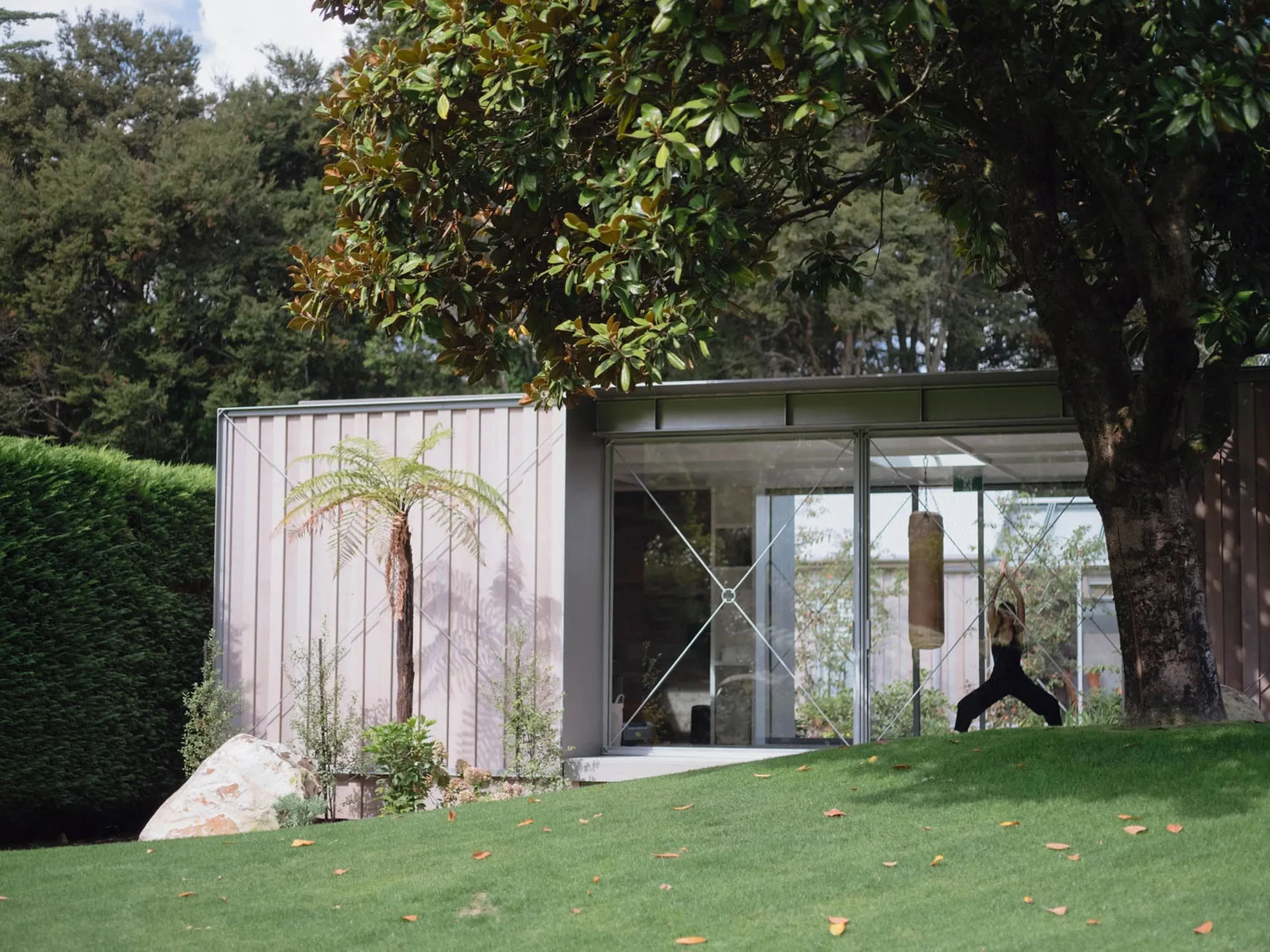 A guest practicing yoga in a modern structure with large glass windows and surrounding greenery.