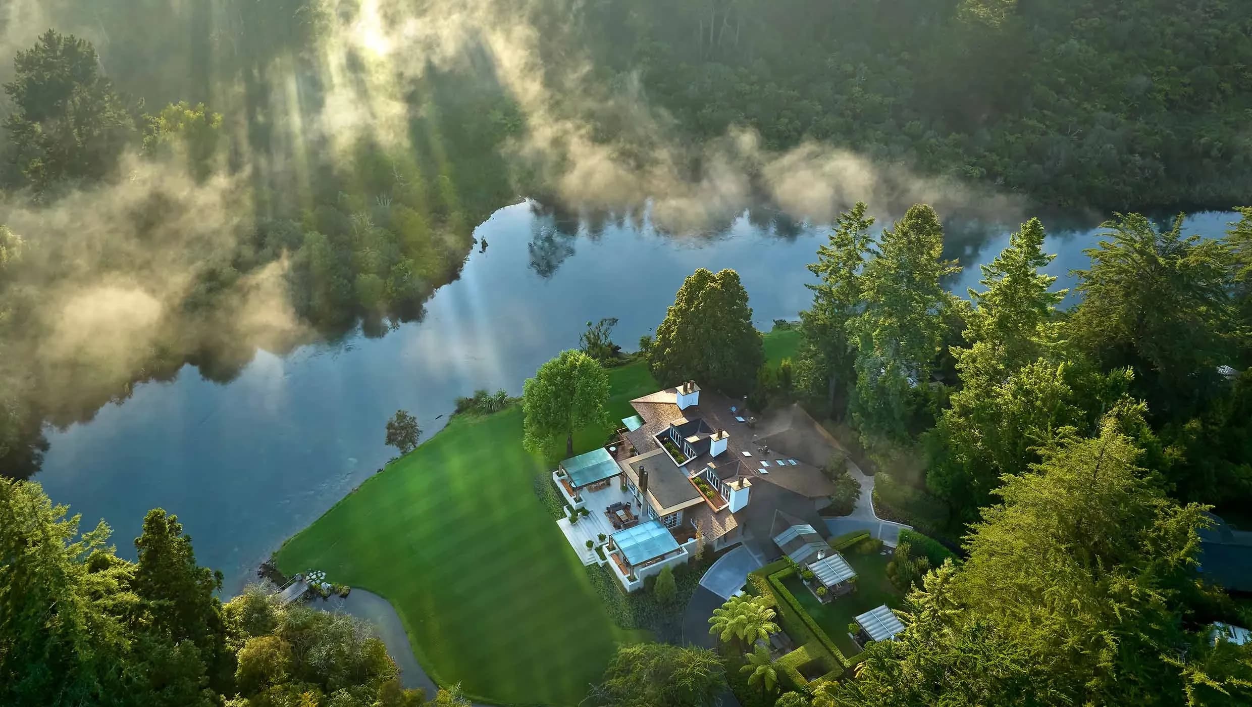 Aerial view of Huka Lodge surrounded by lush greenery and the Waikato River, with mist rising above the water.