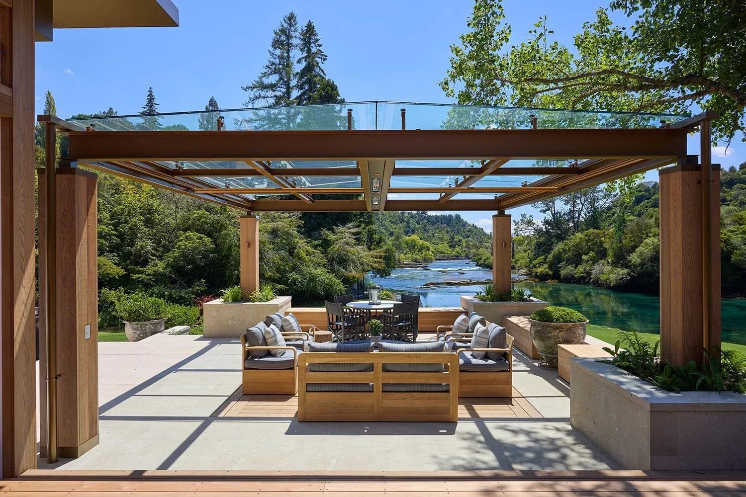 Covered outdoor seating area with timber furniture and cushions, overlooking the river and surrounding greenery.