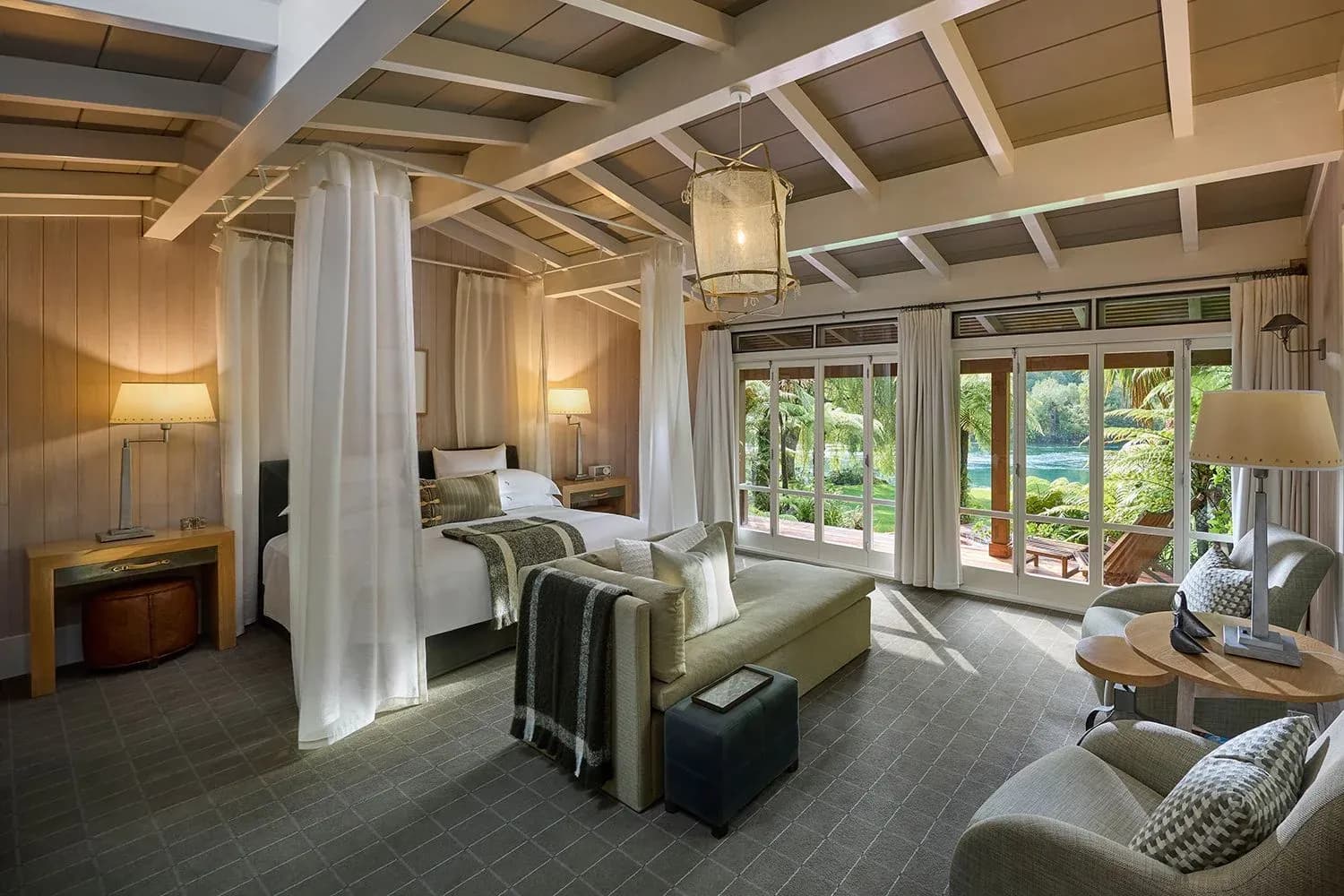 Suite interior with a king bed, seating area, and large windows overlooking lush gardens.