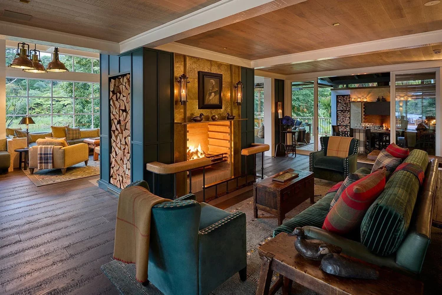 Lounge area with a fireplace, green velvet armchairs, wooden coffee tables, and large windows overlooking the garden.
