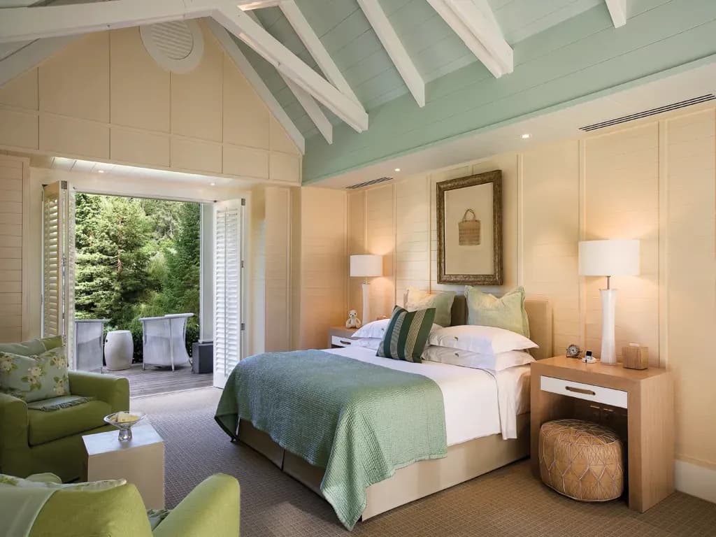 Timber and soft green interior of a suite featuring a made bed, seating area, and outdoor access.