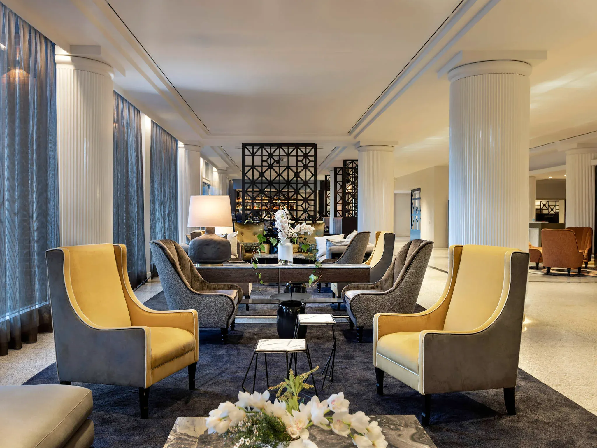 Seating area in lobby with yellow and gray armchairs, decorative tables, and floral arrangements.