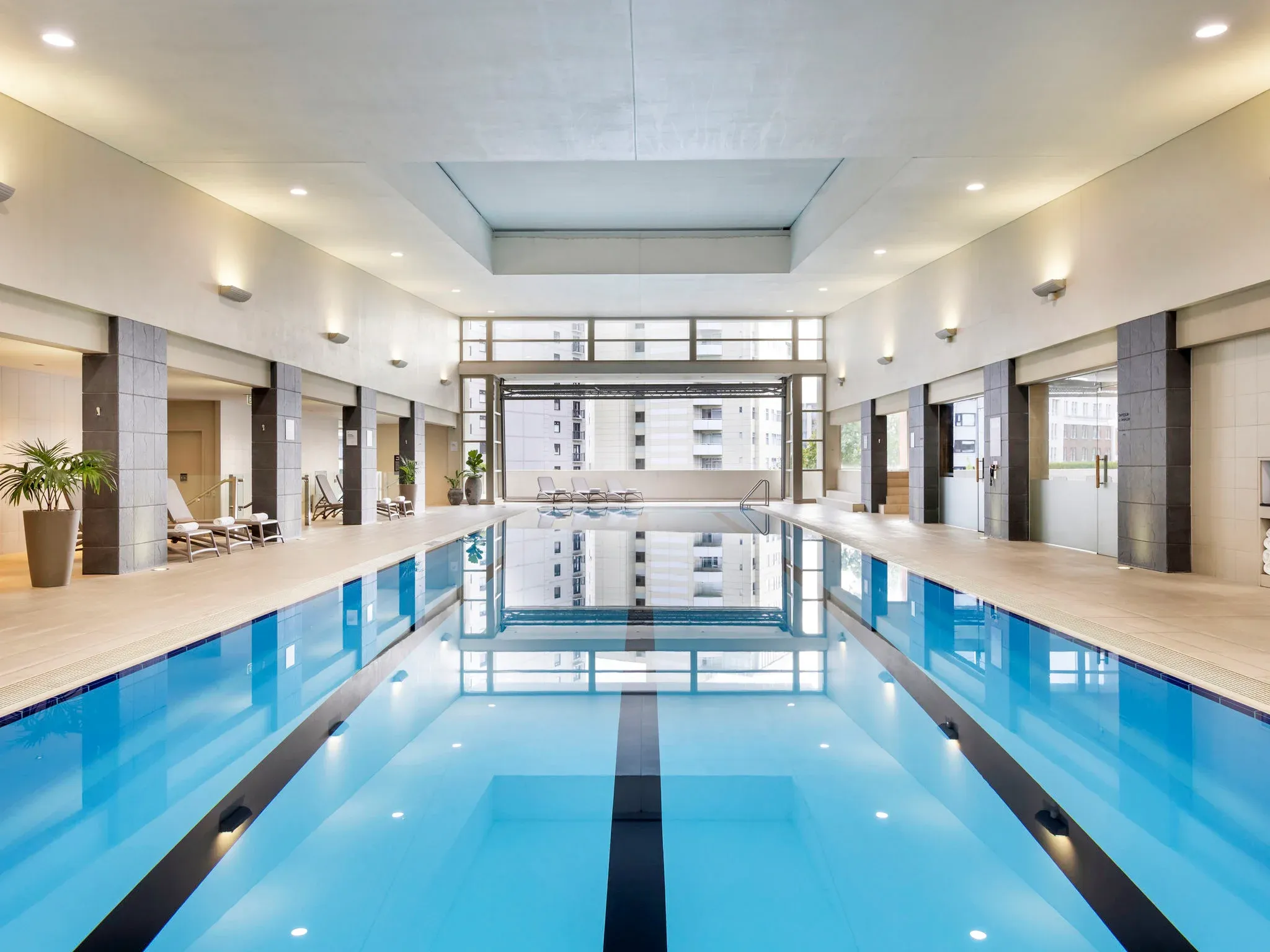 Indoor swimming pool, featuring blue water, tiled edges, and lounge chairs along the sides.