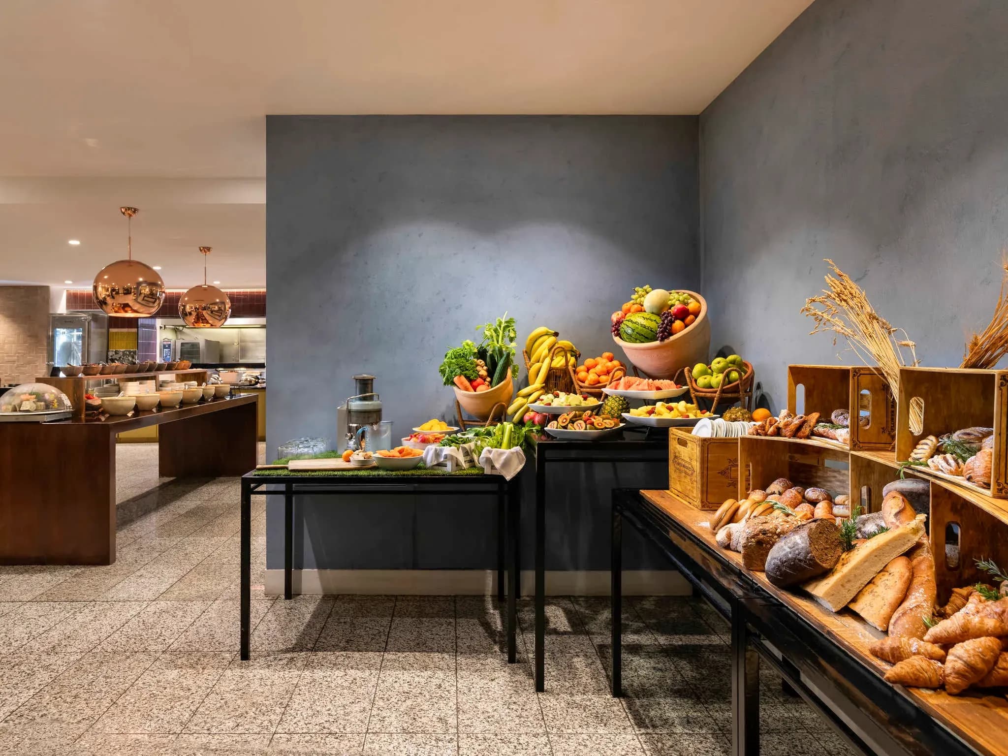 Buffet area with various fresh fruits, vegetables, and baked goods displayed on wooden tables against a blue wall.