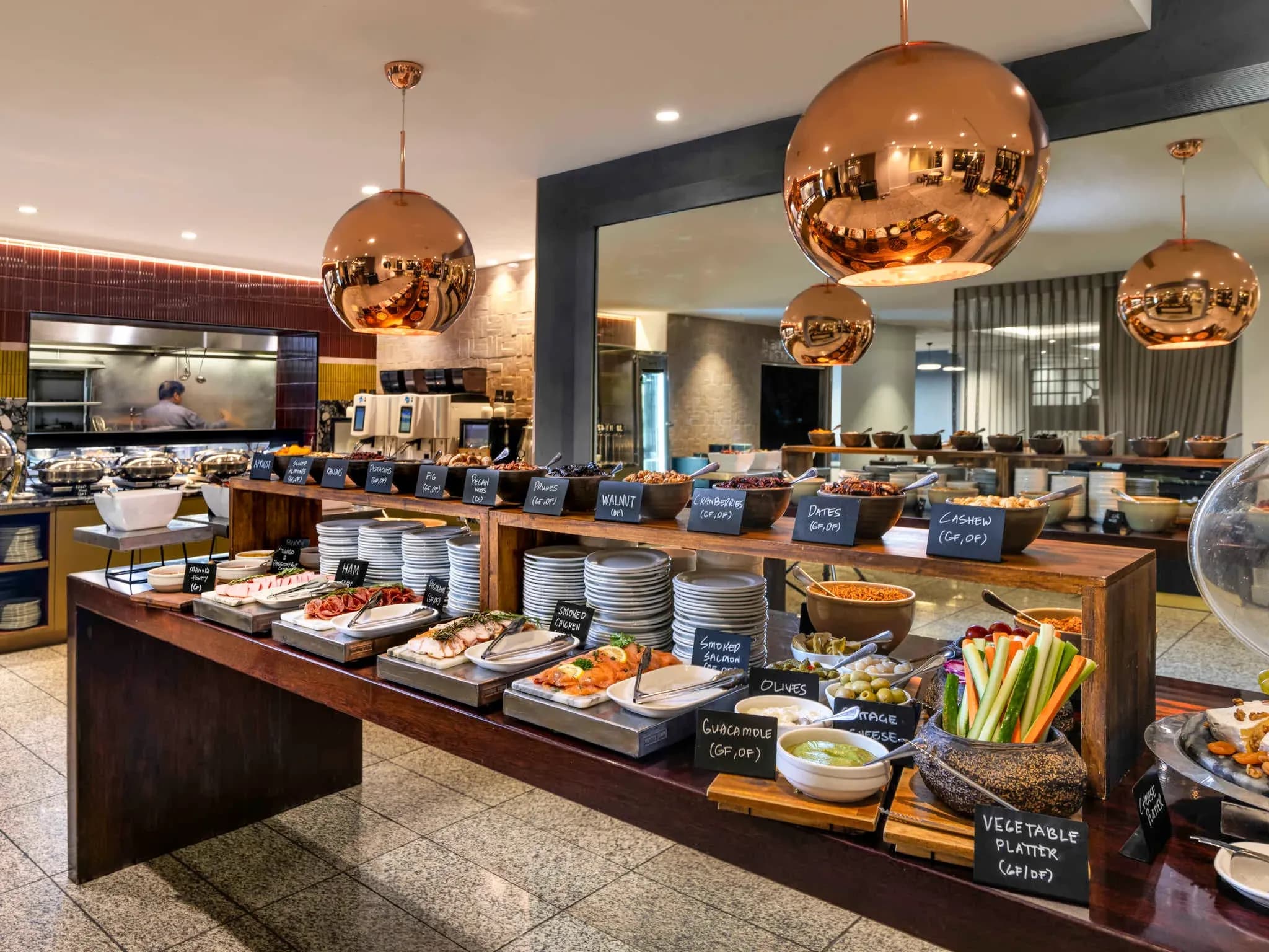Buffet dining area with wooden tables, copper pendant lights, and various food items displayed on trays and bowls.