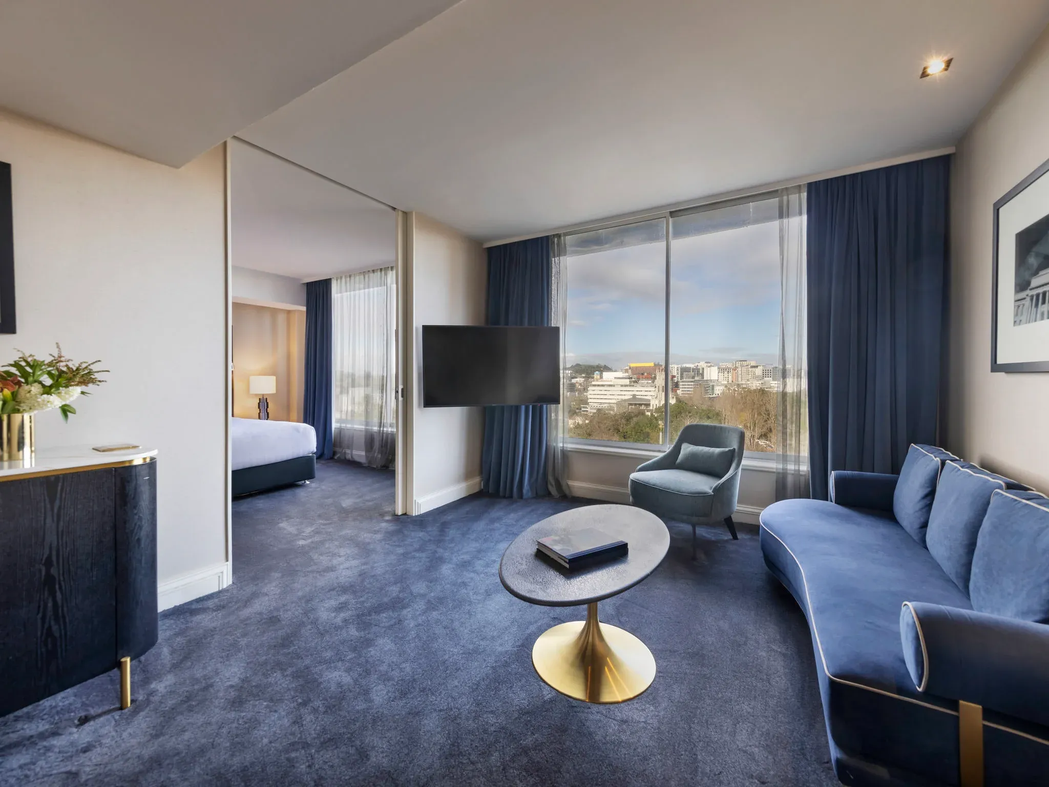 Living area featuring a blue sofa, armchair, round table, and city views through large windows.