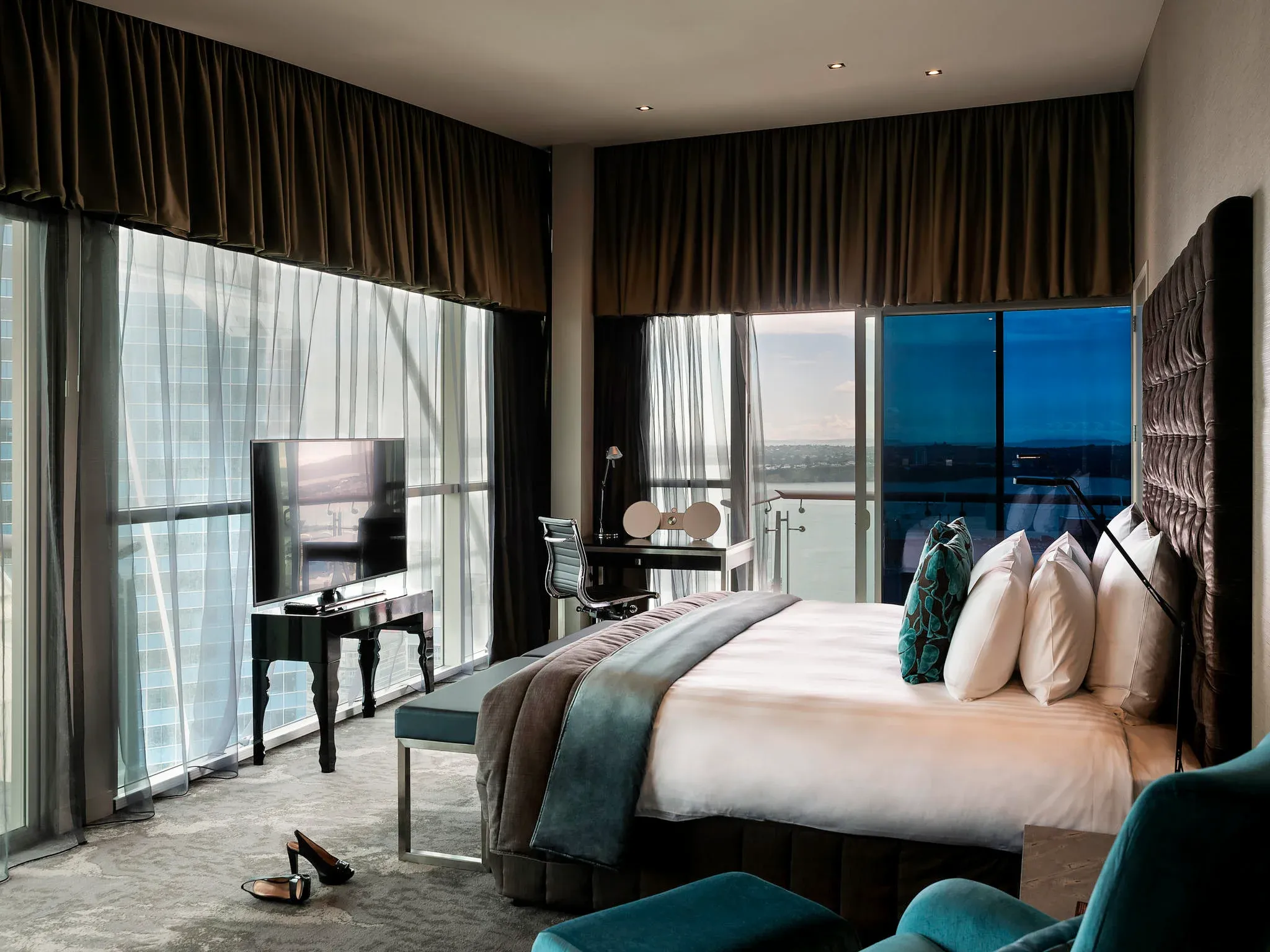Bedroom with a king-size bed, television on a black stand, and a seating area with a view through large windows.