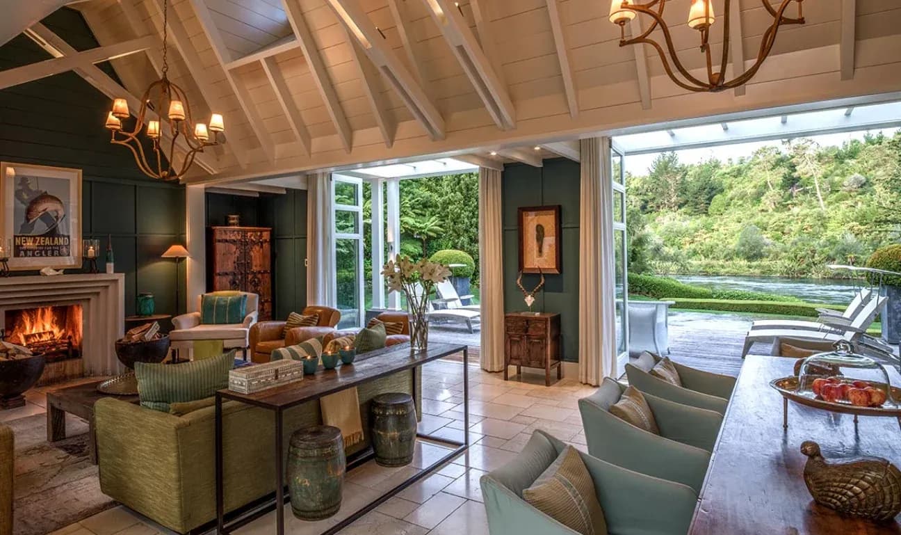 Lounge area featuring a stone fireplace, comfortable seating, and large windows opening to the garden and river.