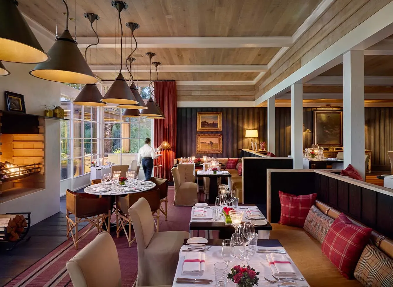 Dining area with wooden ceiling, pendant lights, tables set for meals, and a fireplace.
