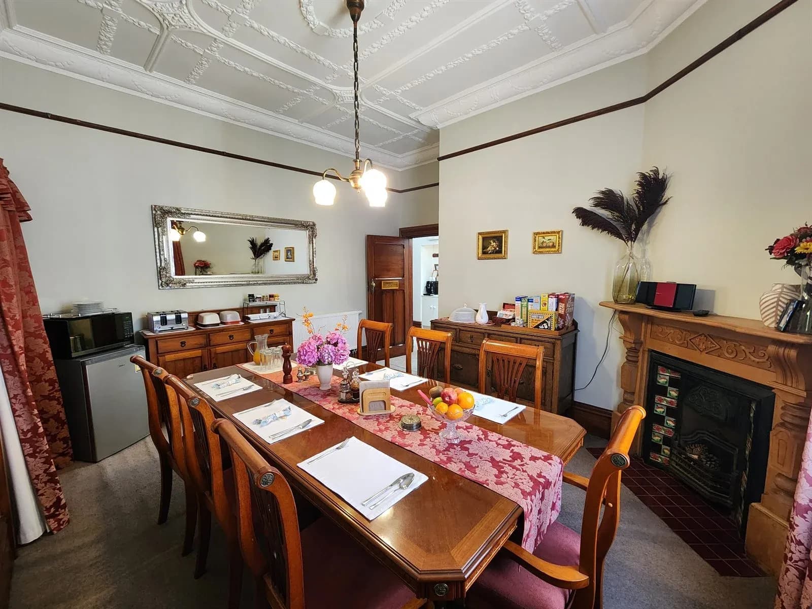 Dining room at The Fern & Thistle featuring a wooden table set for eight, a mirror, and a fireplace with decorative elements.