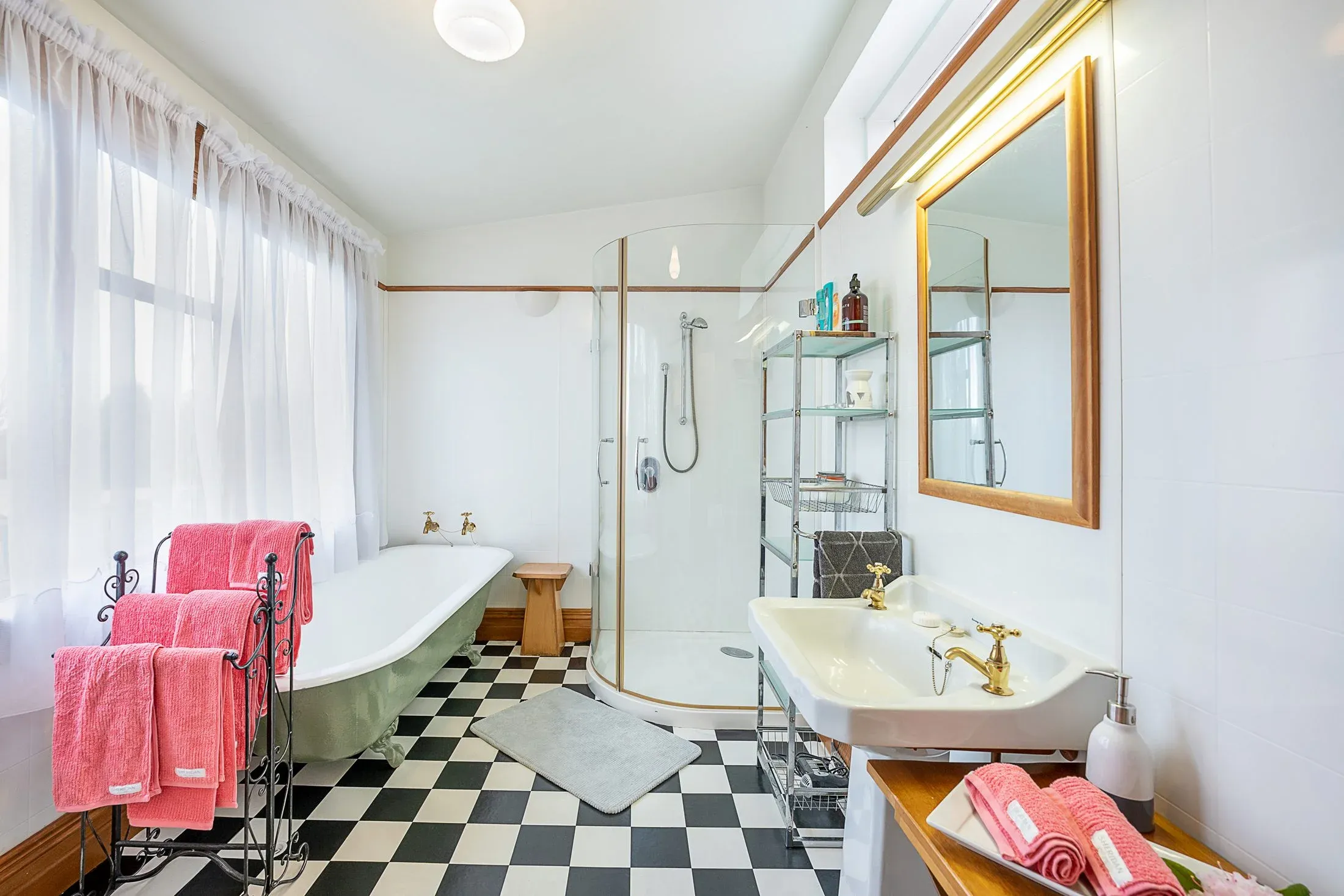Bathroom with a freestanding bathtub, glass shower, and black and white checkered floor, featuring pink towels and a wooden shelf.