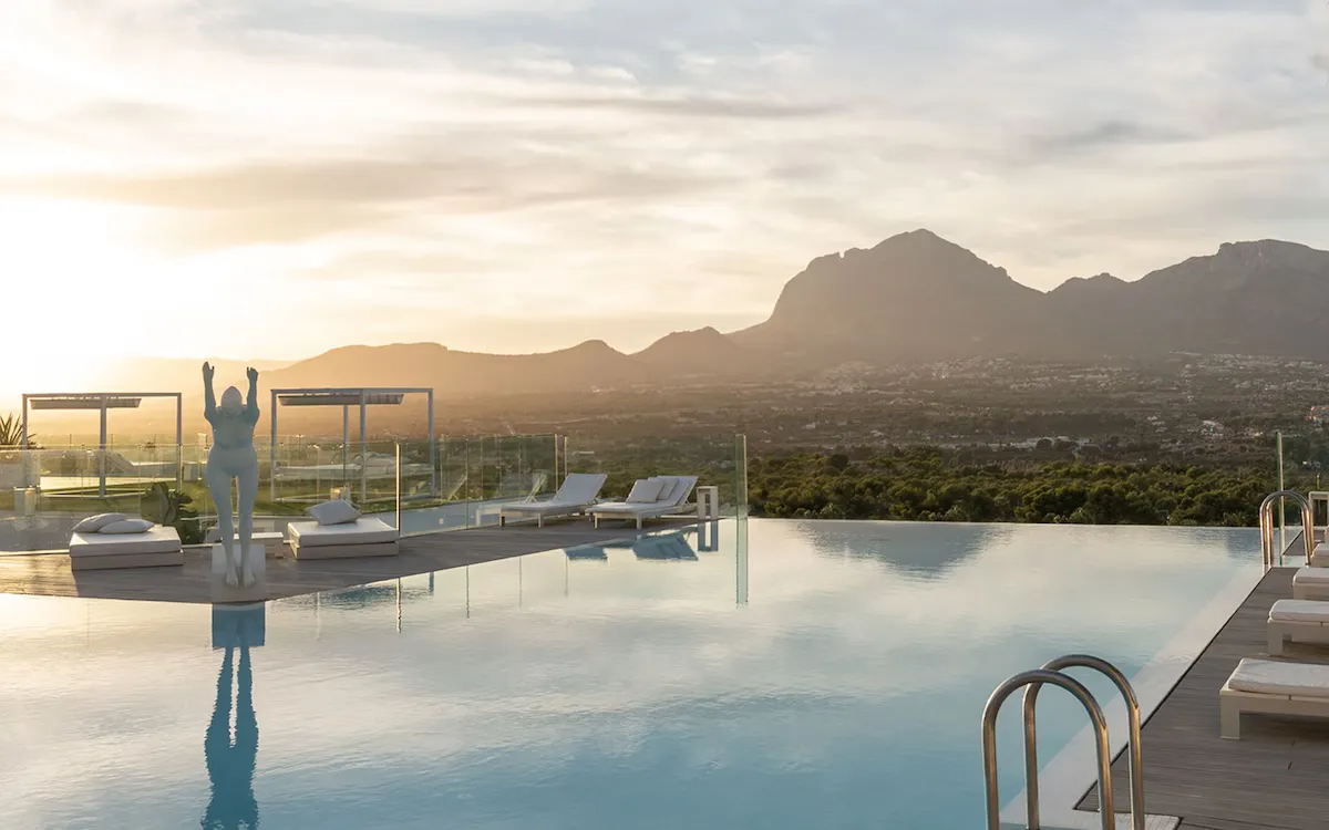 Poolside area at SHA Spain with a white sculpture, sun loungers, and mountains in the background at sunset.