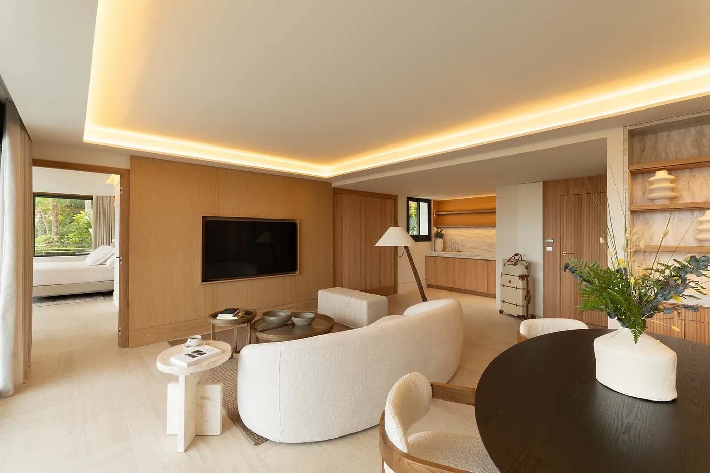 Living area with a curved white sofa, dark round table, wall-mounted television, and wooden cabinetry.