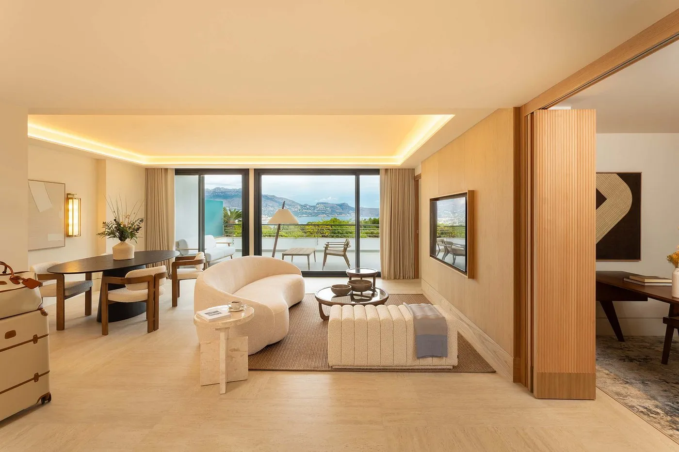 Living area with curved sofa, dining table, and mountain views through glass doors at SHA Spain.