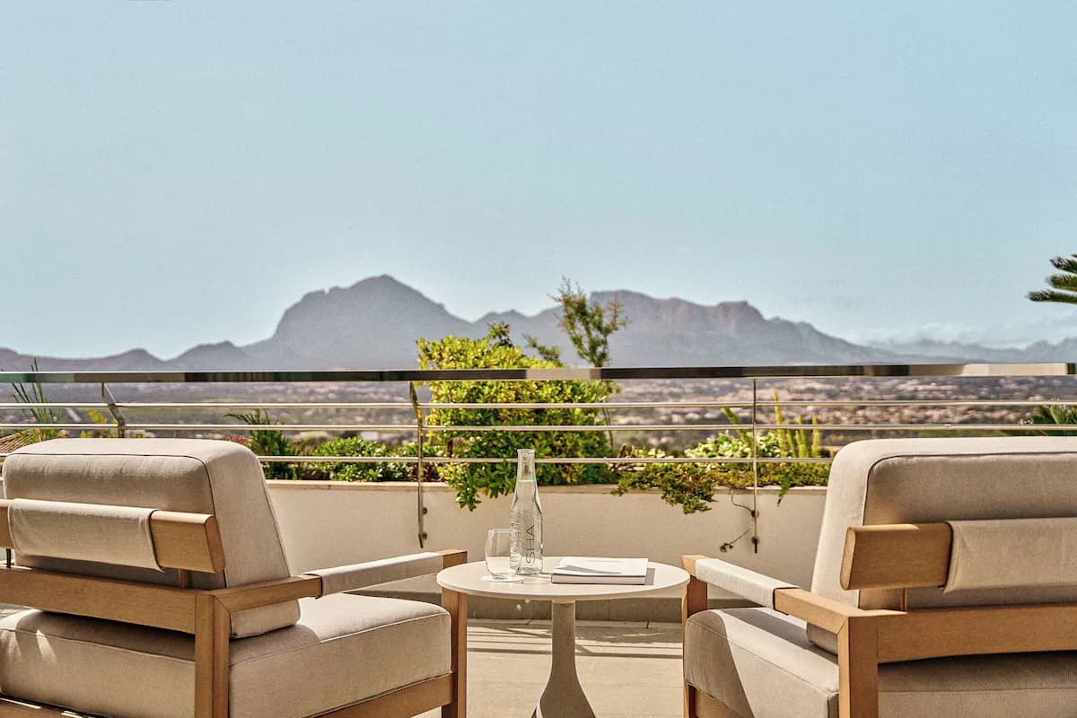 Two armchairs with soft cushions facing a small table, overlooking mountainous landscape and greenery.