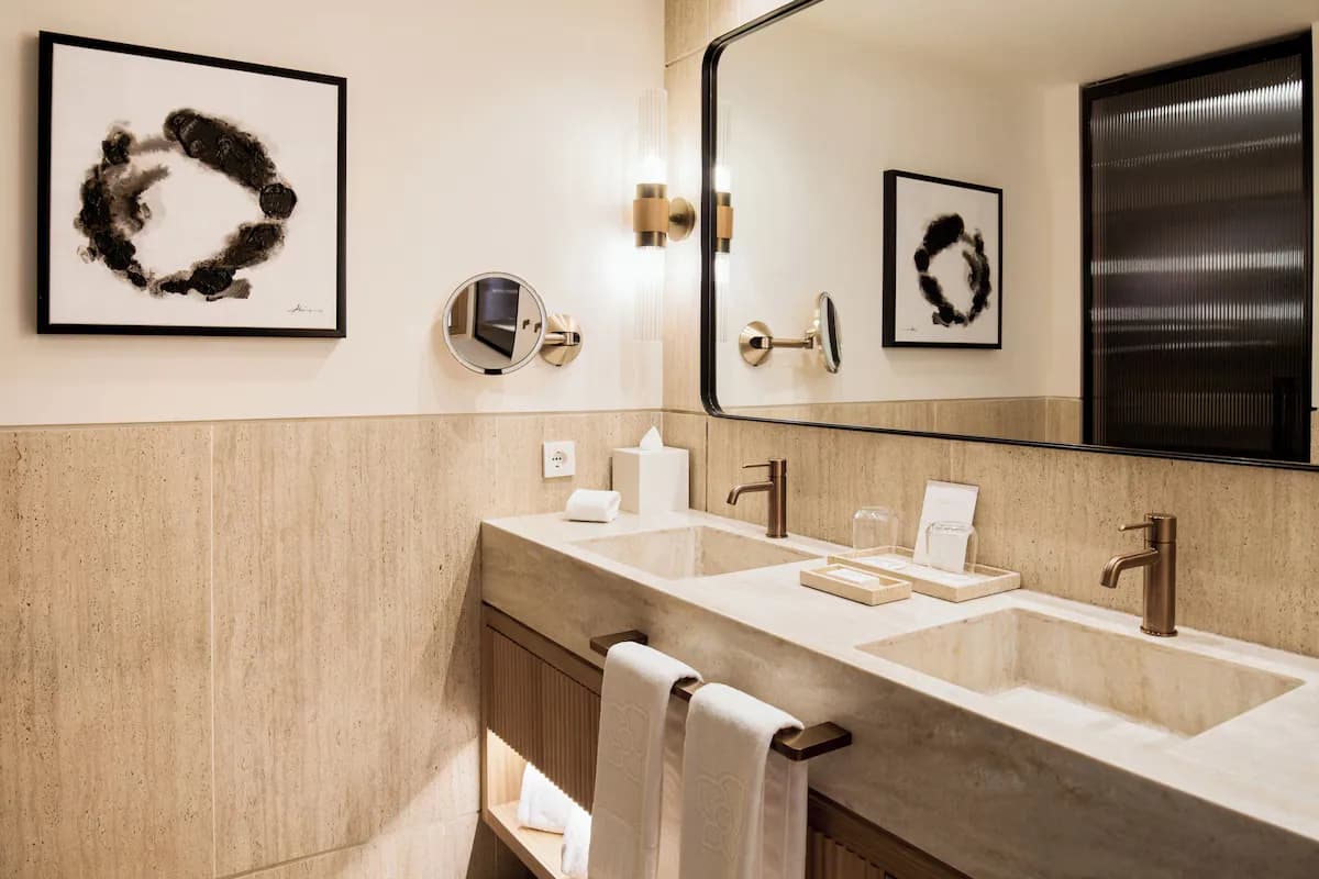 Bathroom interior featuring dual sinks with bronze faucets, stone countertop, mirror, and abstract art on the wall.