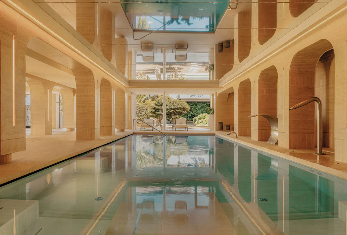 Indoor swimming pool with stone walls, arched openings, and lounge chairs visible through large windows.
