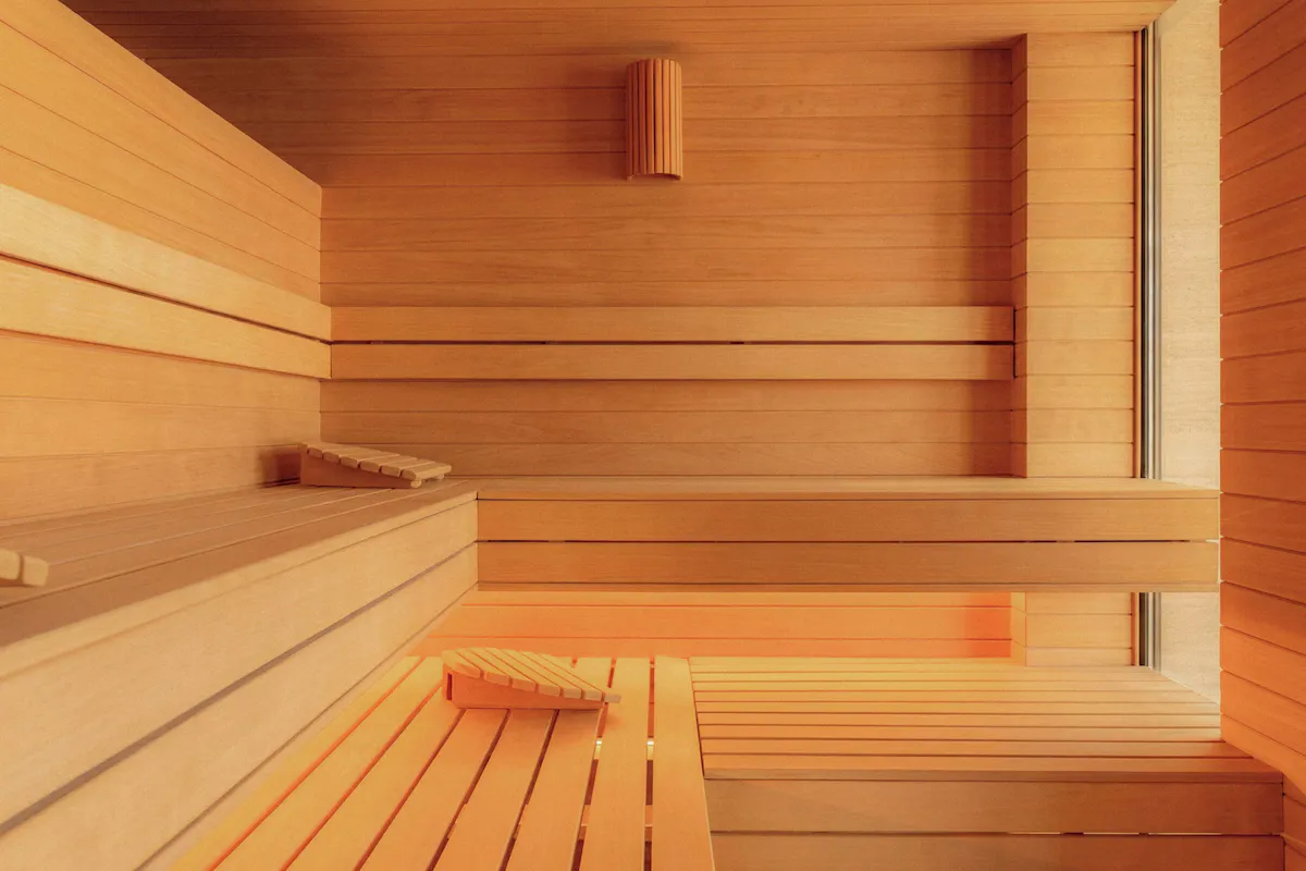 Timber sauna interior with wooden benches, warm ambient light, and a simple wooden light fixture.