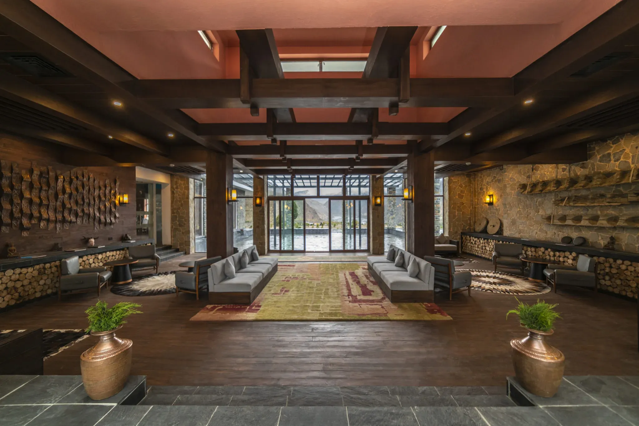 Lounge area with wooden beams, stone walls, seating arrangements, and a view of the outdoors at Shinta Mani Mustang.