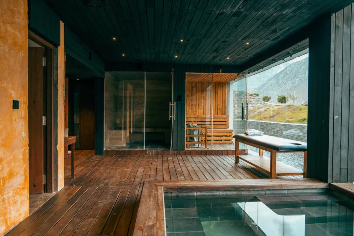 Sauna and steam room area with wooden benches, glass walls, dark timber flooring and a hot tub.