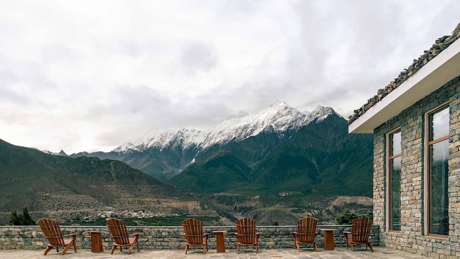 Stone terrace with wooden chairs overlooking snow-capped mountains and a valley at Shinta Mani Mustang.