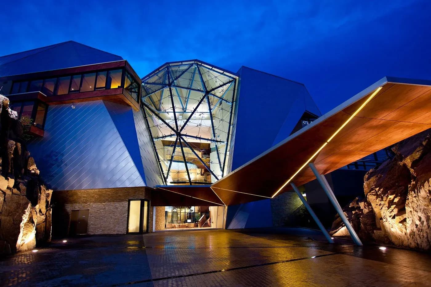 Exterior view of Sparkling Hill Resort featuring angular architecture, large glass panels, and illuminated entryway at dusk.