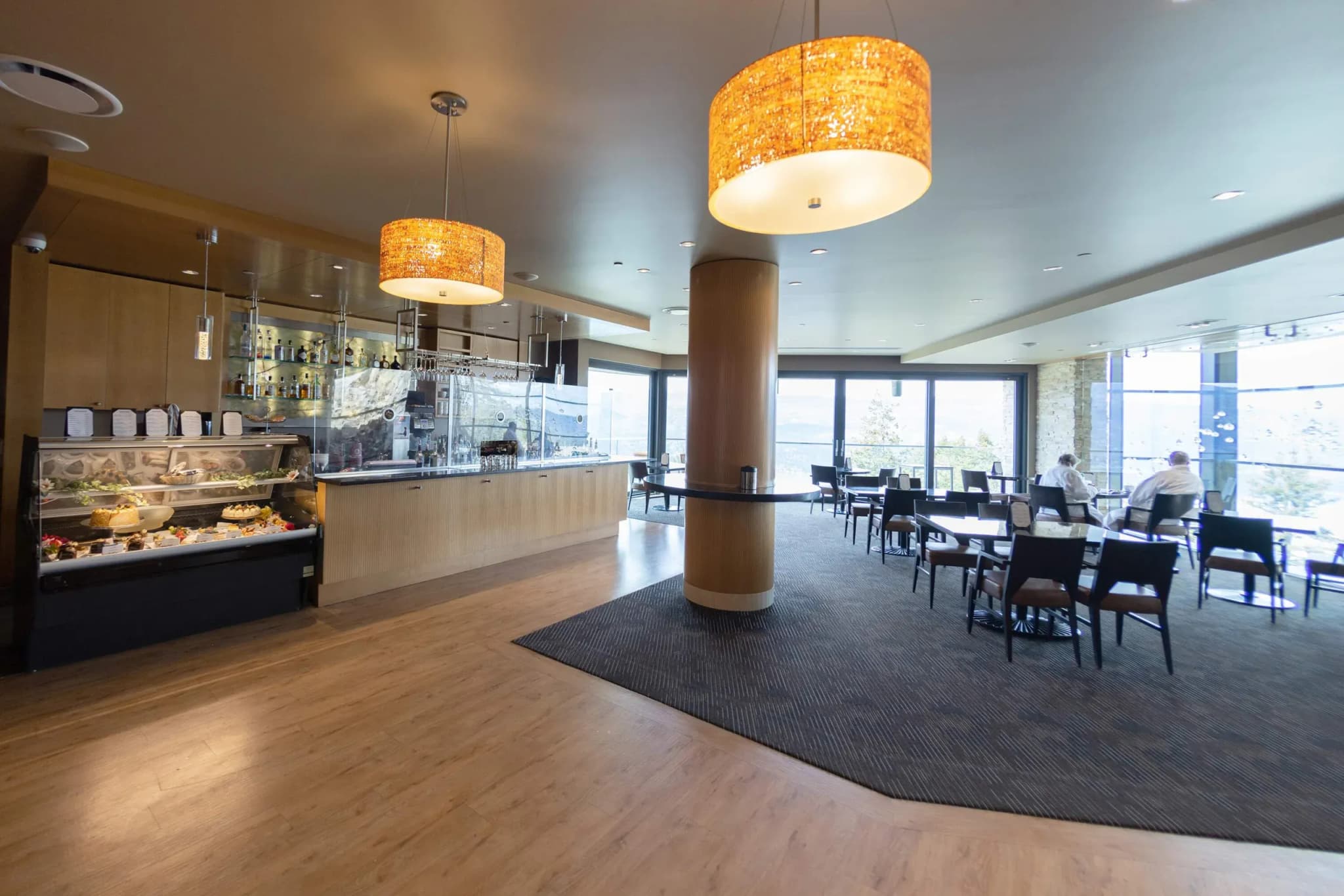 Bar area with a display of food, wooden counter, and two large pendant lights in a dining space.