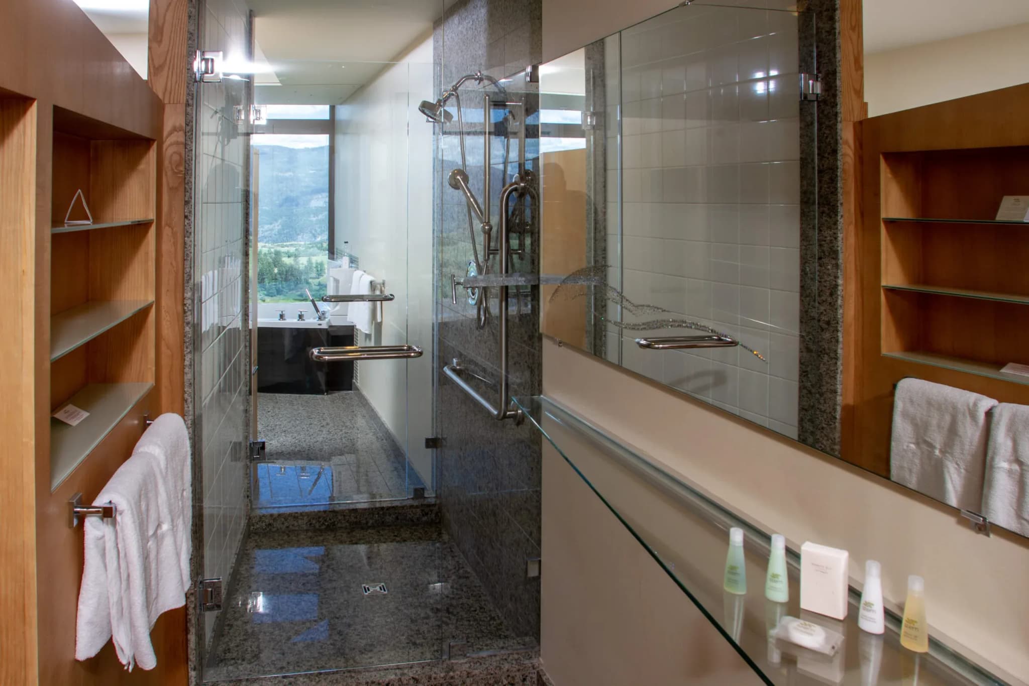 Bathroom interior featuring a glass shower, granite surfaces, and a view of the surrounding landscape.