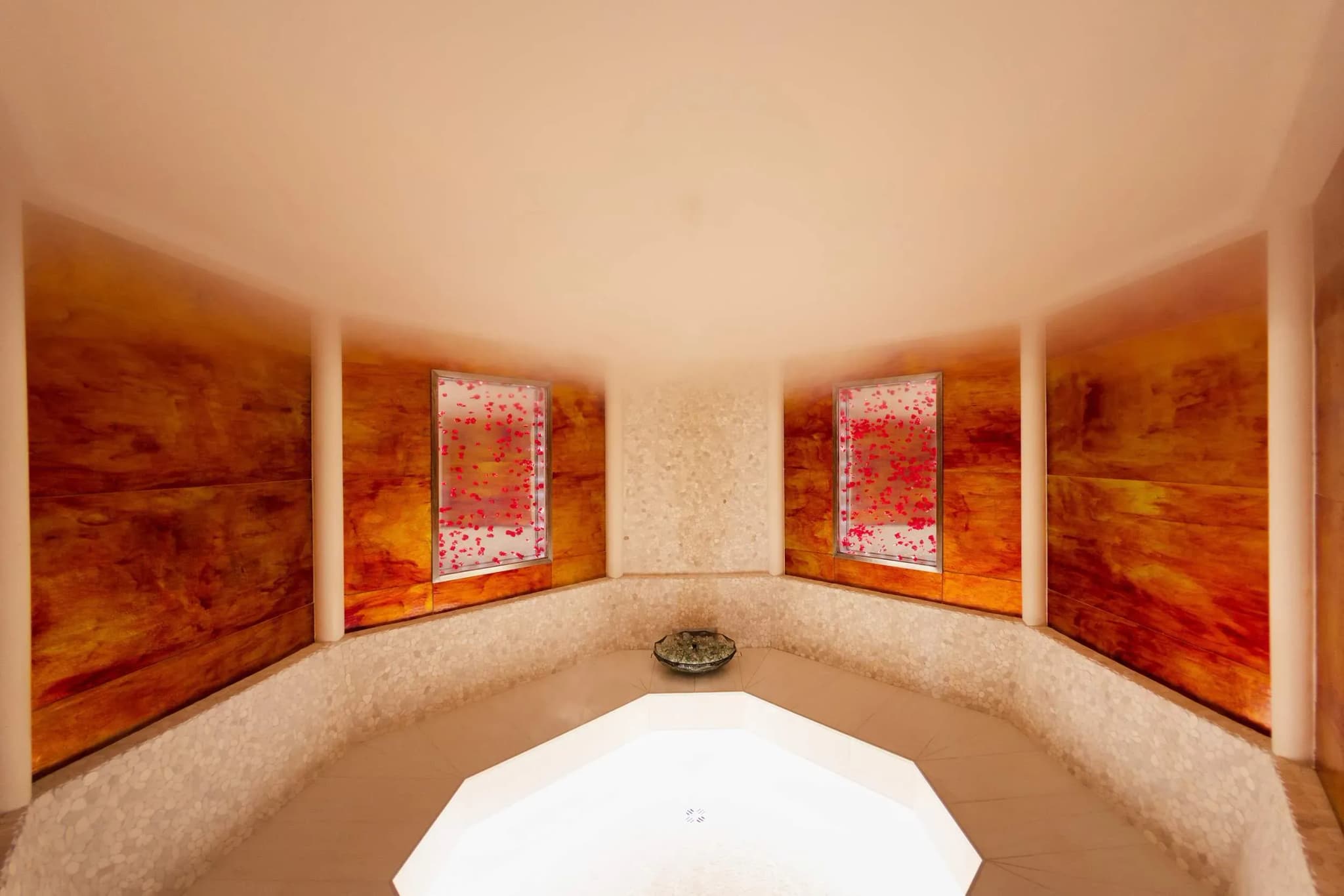 Curved seating area in steam room with warm wood paneling and a stone basin at Sparkling Hill Resort's wellness facility.