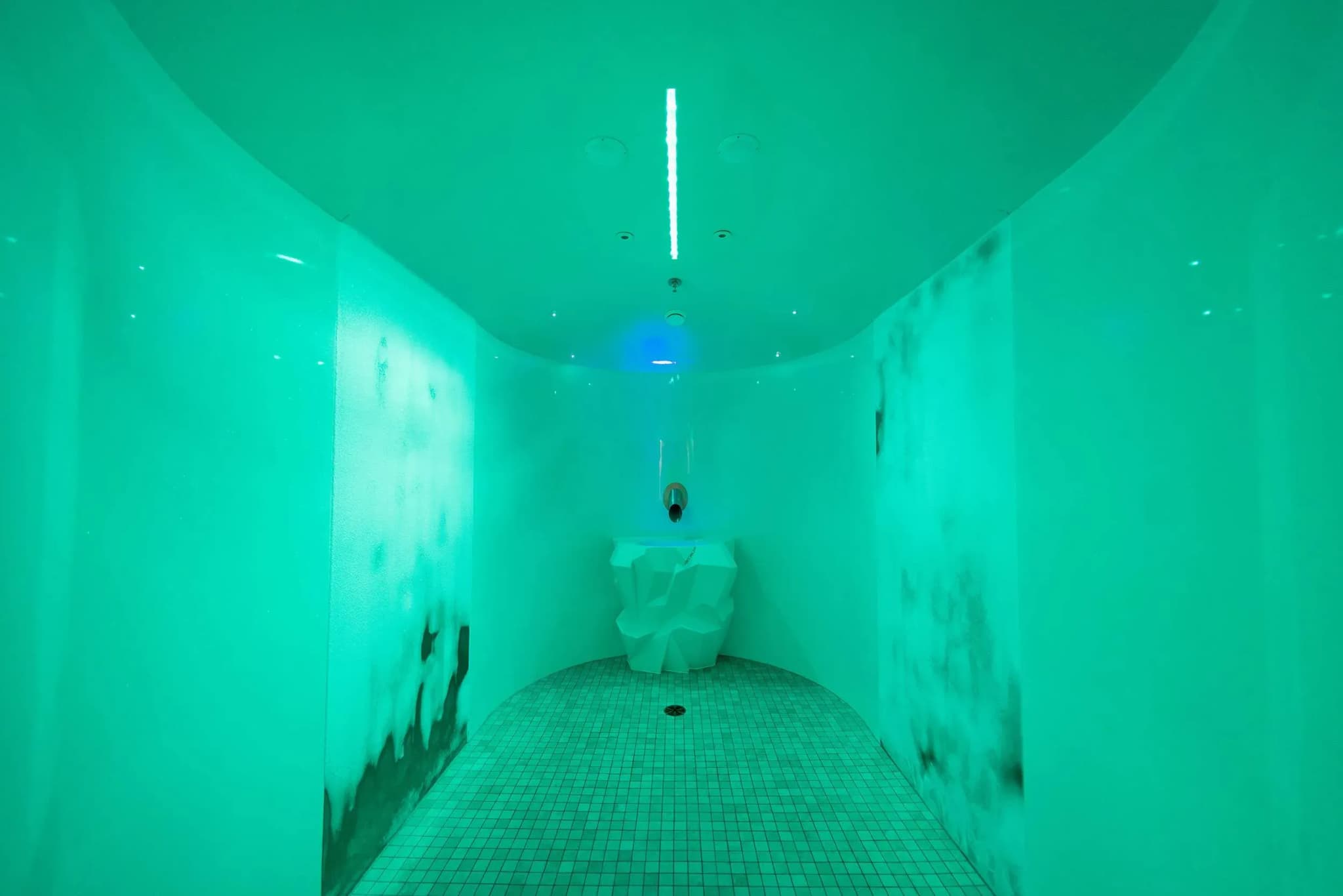 Curved cold room with green ambient lighting, textured walls, and a sculptural feature in the center.