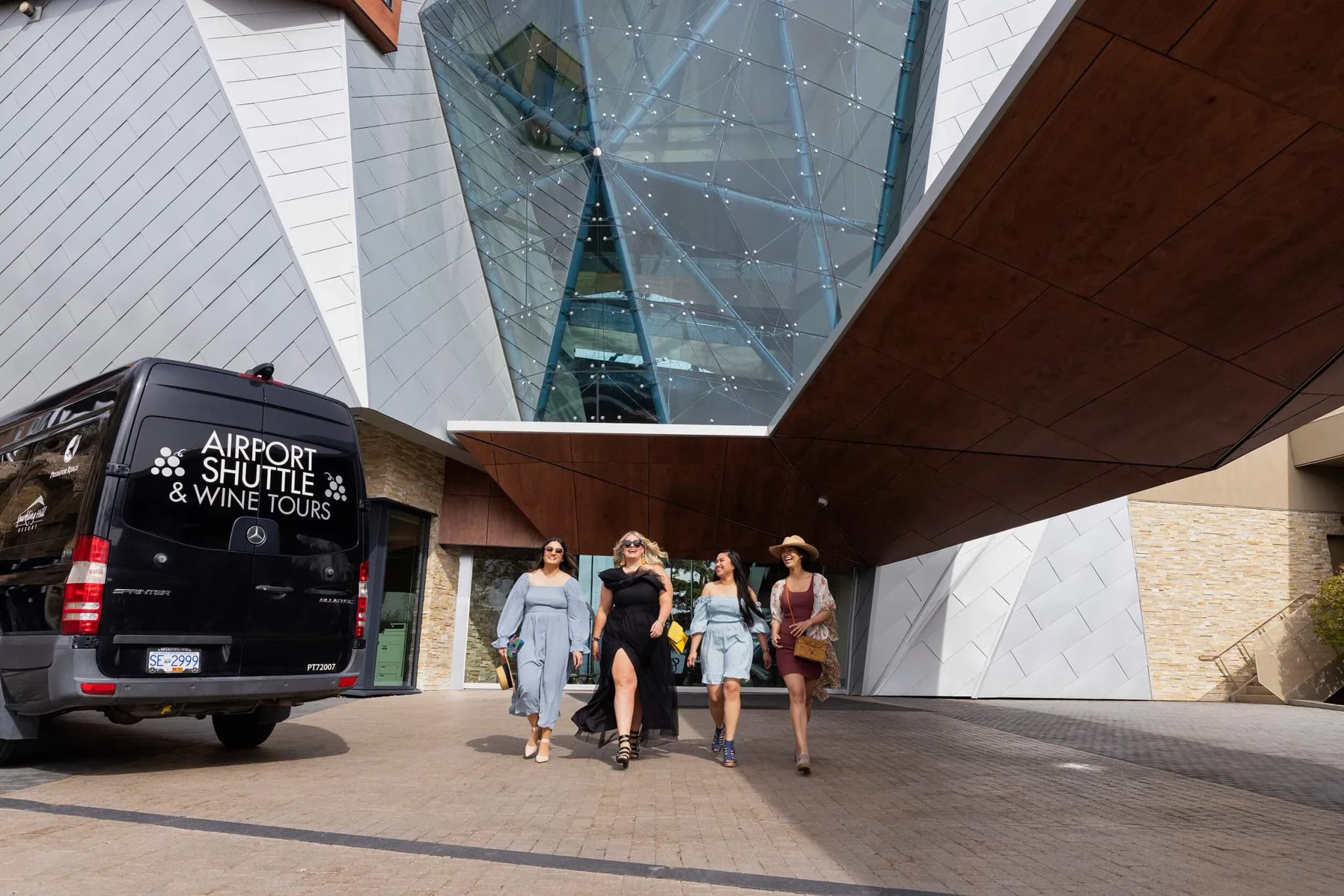 Guests walking towards Sparkling Hill Resort, with a black shuttle van parked nearby and modern architectural features in the background.