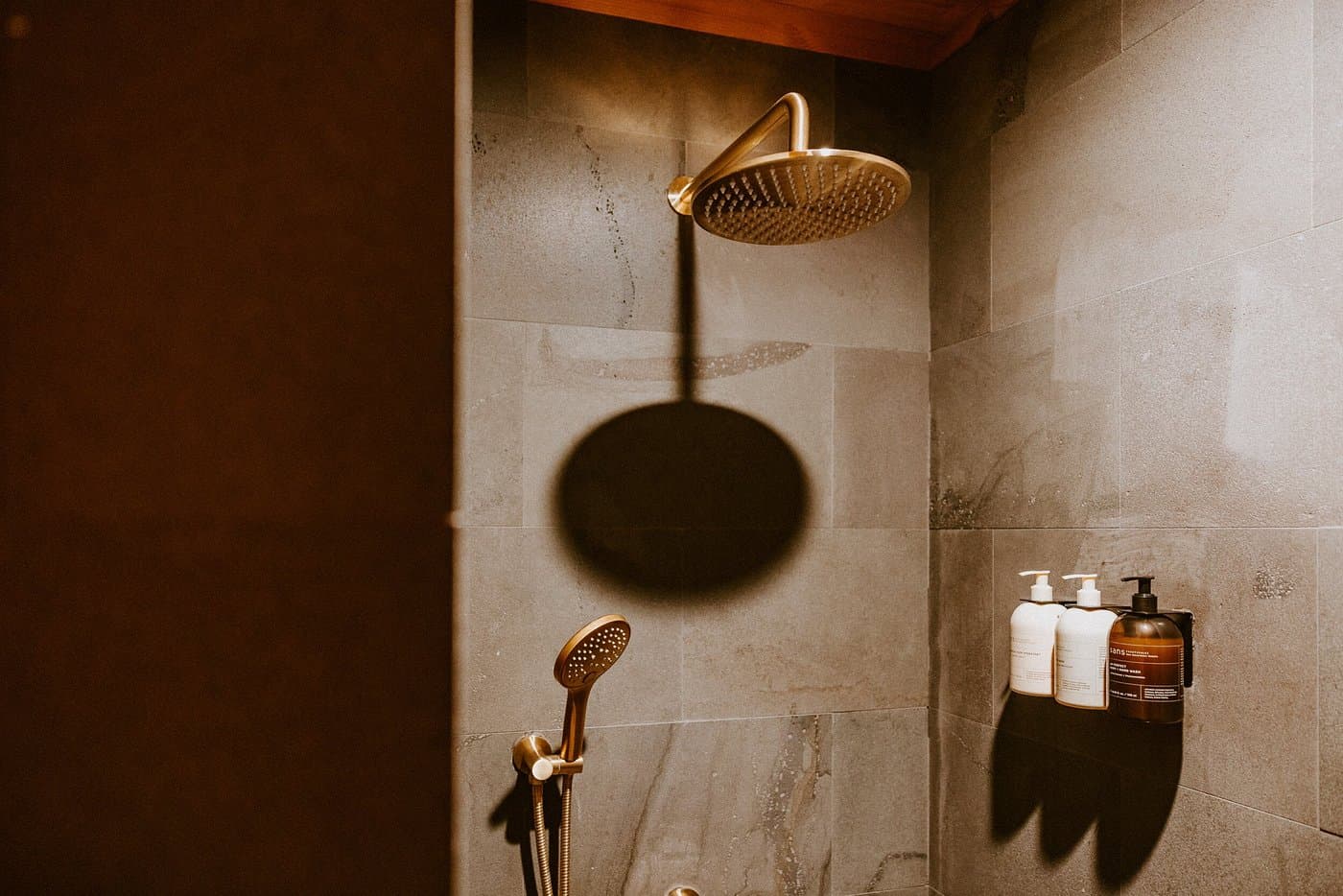 Stone-tiled shower with rainfall shower head, handheld shower and wall-mounted bath products.