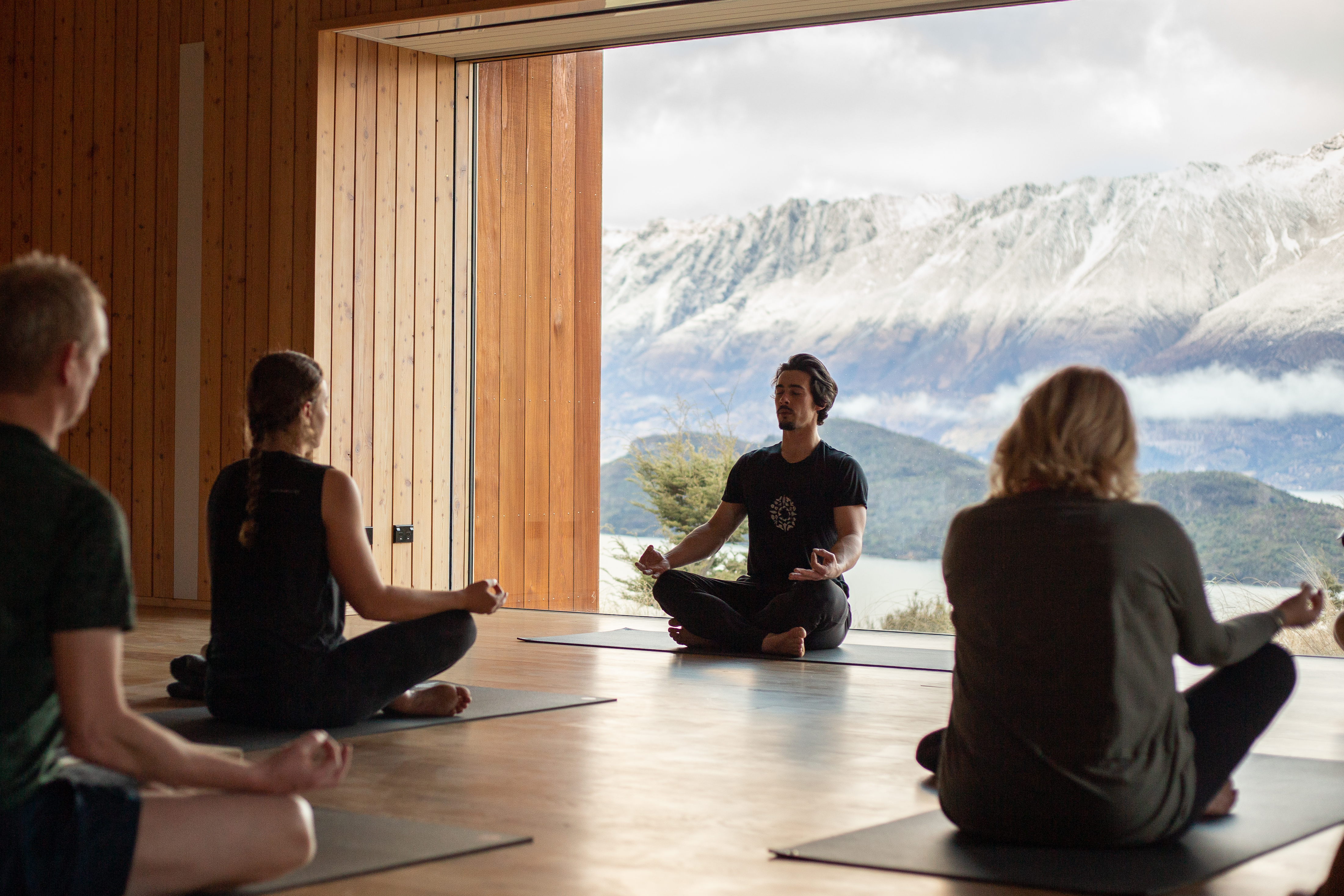Meditation and breathwork session inside a timber-lined wellness studio overlooking snow-covered mountains.