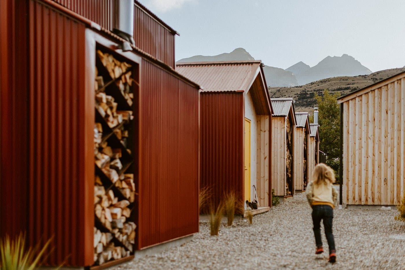 Timber alpine huts with stacked firewood, gravel paths and mountain views at The Great Glenorchy Alpine Base Camp.
