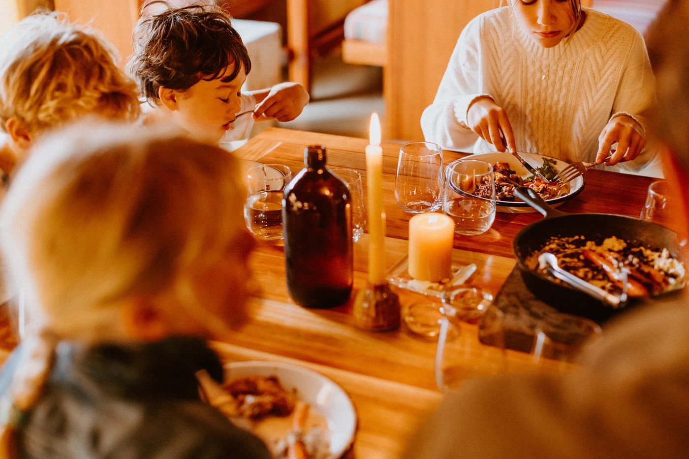 Children eating dinner by candlelight at a timber table inside The Great Glenorchy Alpine Base Camp.