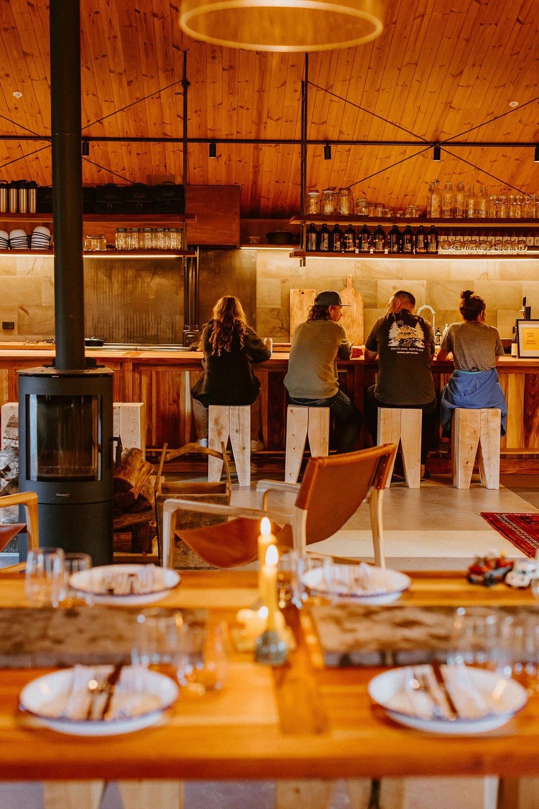 Guests seated at the Base Camp Kitchen bar, with timber interiors, open shelving and a wood-burning fire.