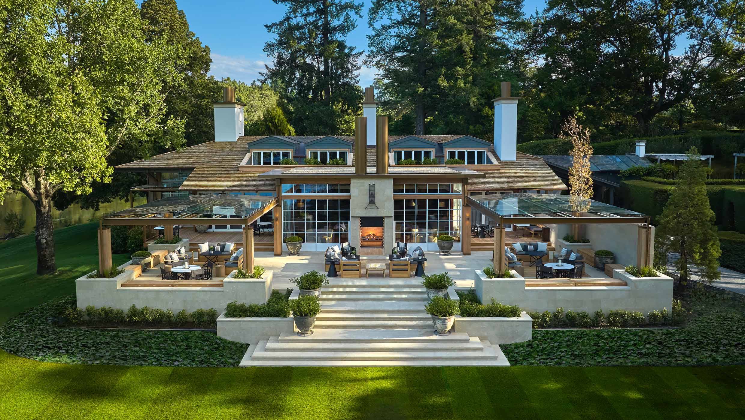 Lodge exterior featuring a stone terrace, outdoor seating, and large windows, surrounded by greenery and trees.