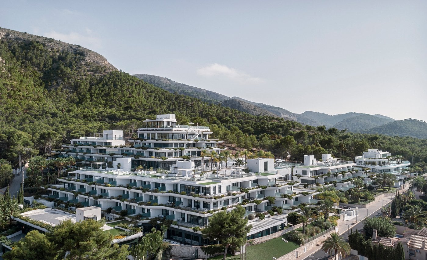 Modern white building complex on a hillside surrounded by greenery and distant mountains at SHA Spain.