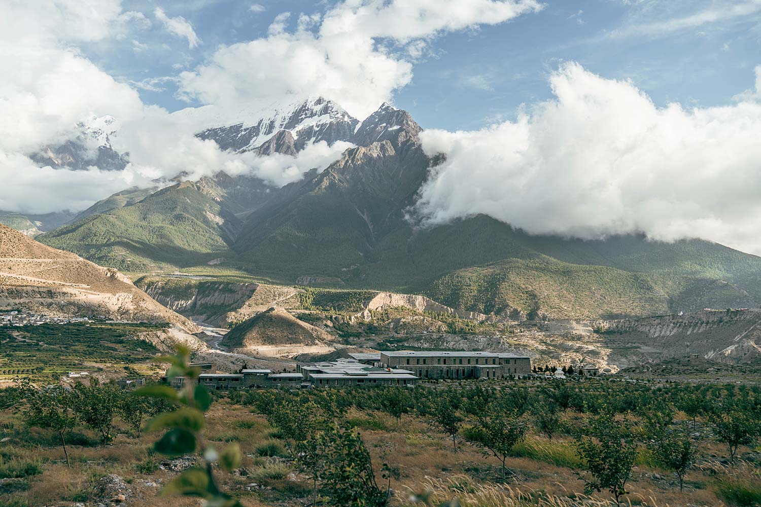 Mountainous landscape with snow-capped peaks and rolling hills, featuring Shinta Mani Mustang nestled among greenery.