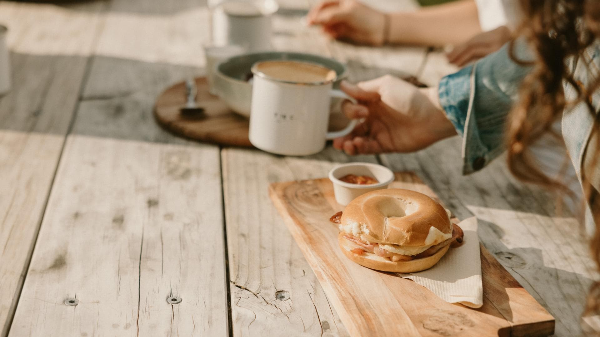 Bagel, coffee and breakfast served on a timber outdoor table at The Camp Lake Hāwea.