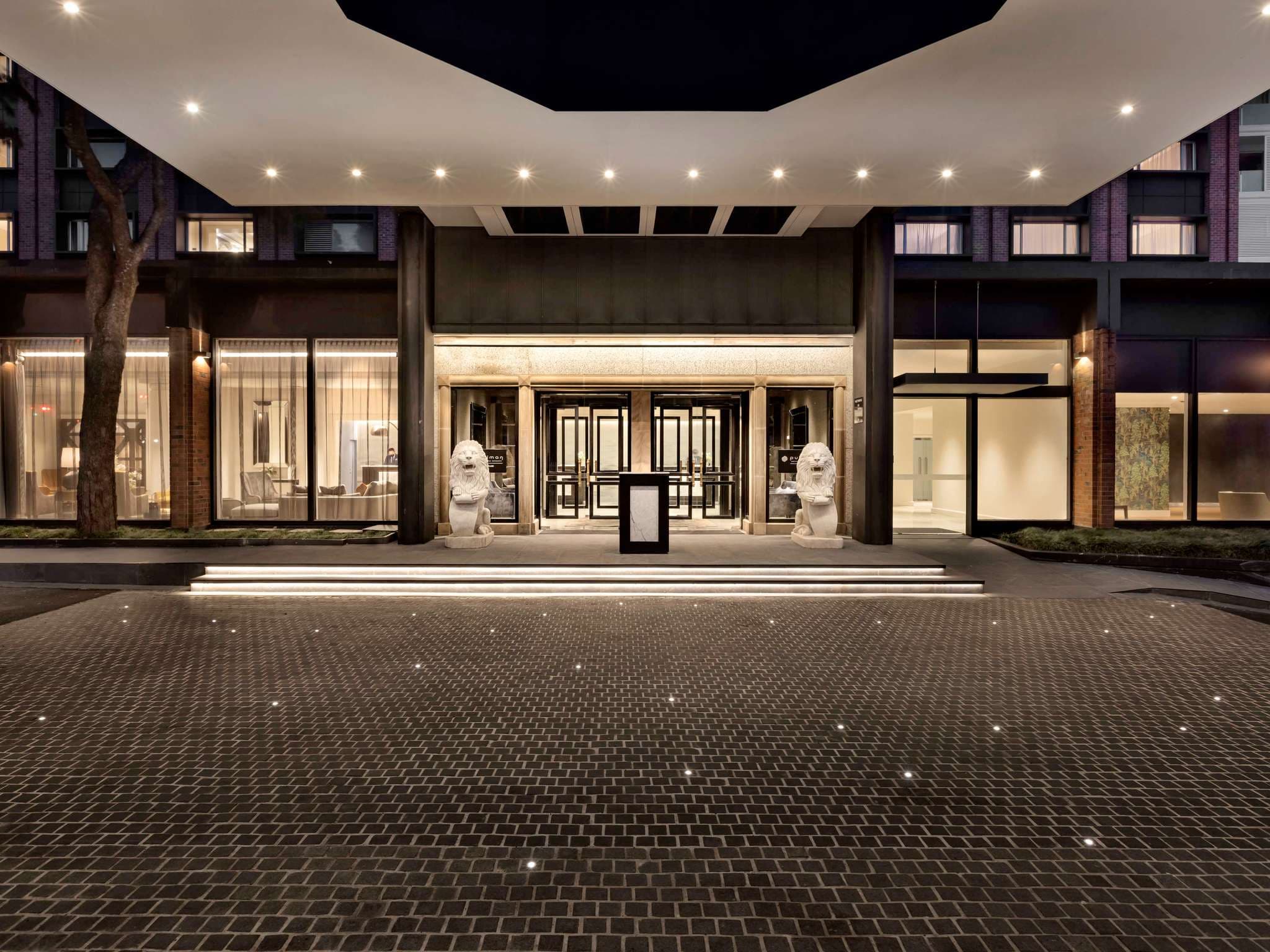 Entrance to Pullman Auckland Hotel & Apartments featuring stone lion statues, glass doors, and patterned paving under ambient lighting.