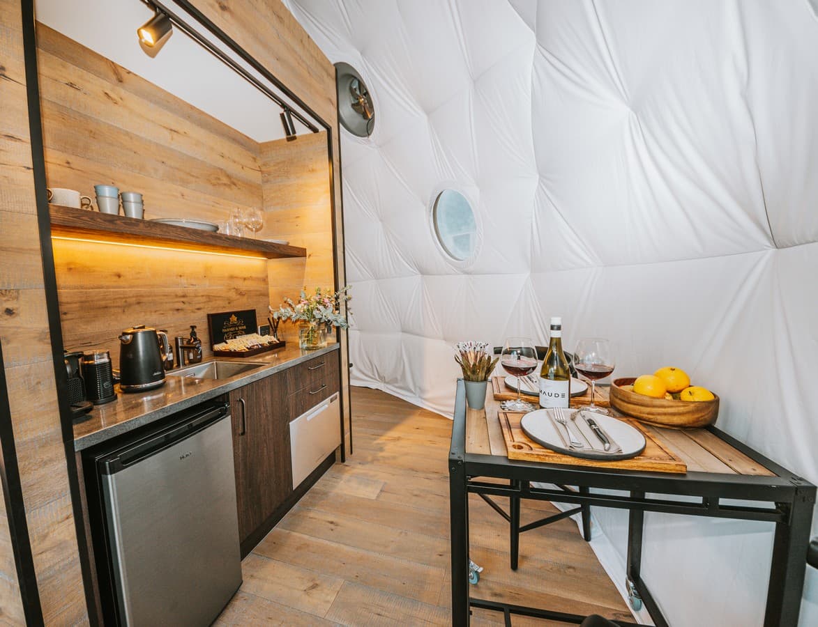 Cross Hill Geo Dome kitchenette and dining area with wine, fruit, timber finishes and soft lighting.
