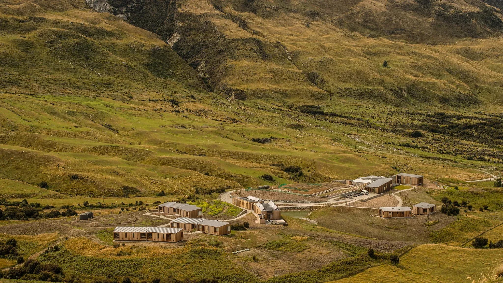 Aro Ha retreat set in a green valley surrounded by rolling hills and mountains, with wooden buildings and pathways.