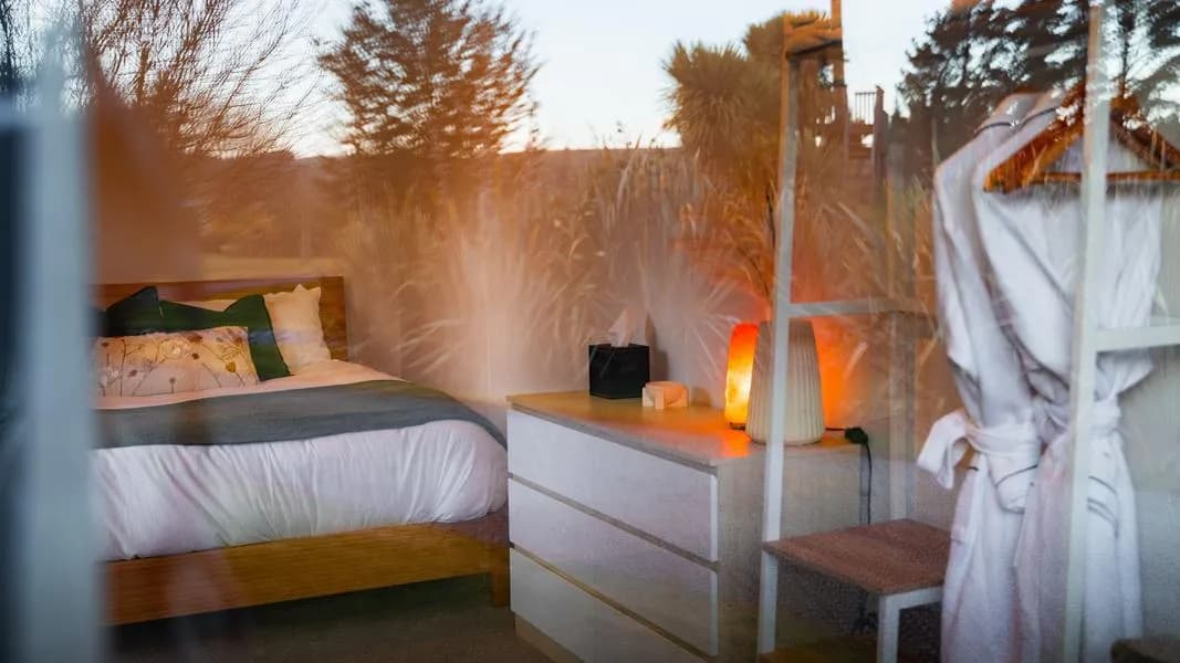 Bedroom with a wooden bed, white bedding, dresser, and soft lighting from a lamp and salt lamp.