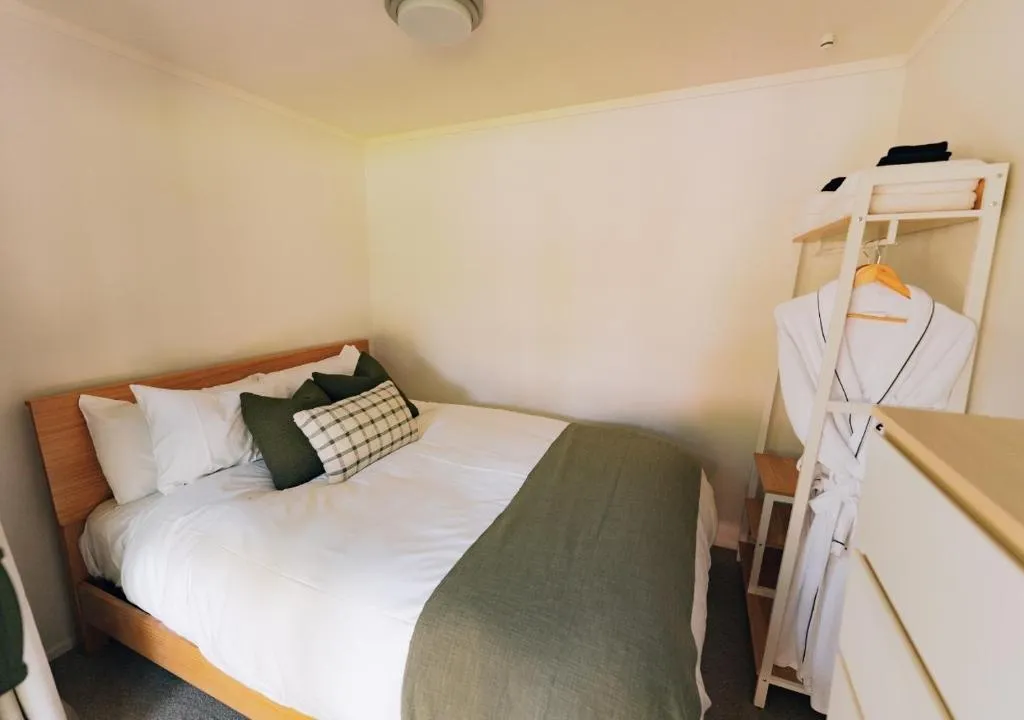 Bedroom with a wooden bed, white bedding, green throw, and a plaid cushion, alongside a robe and storage unit.