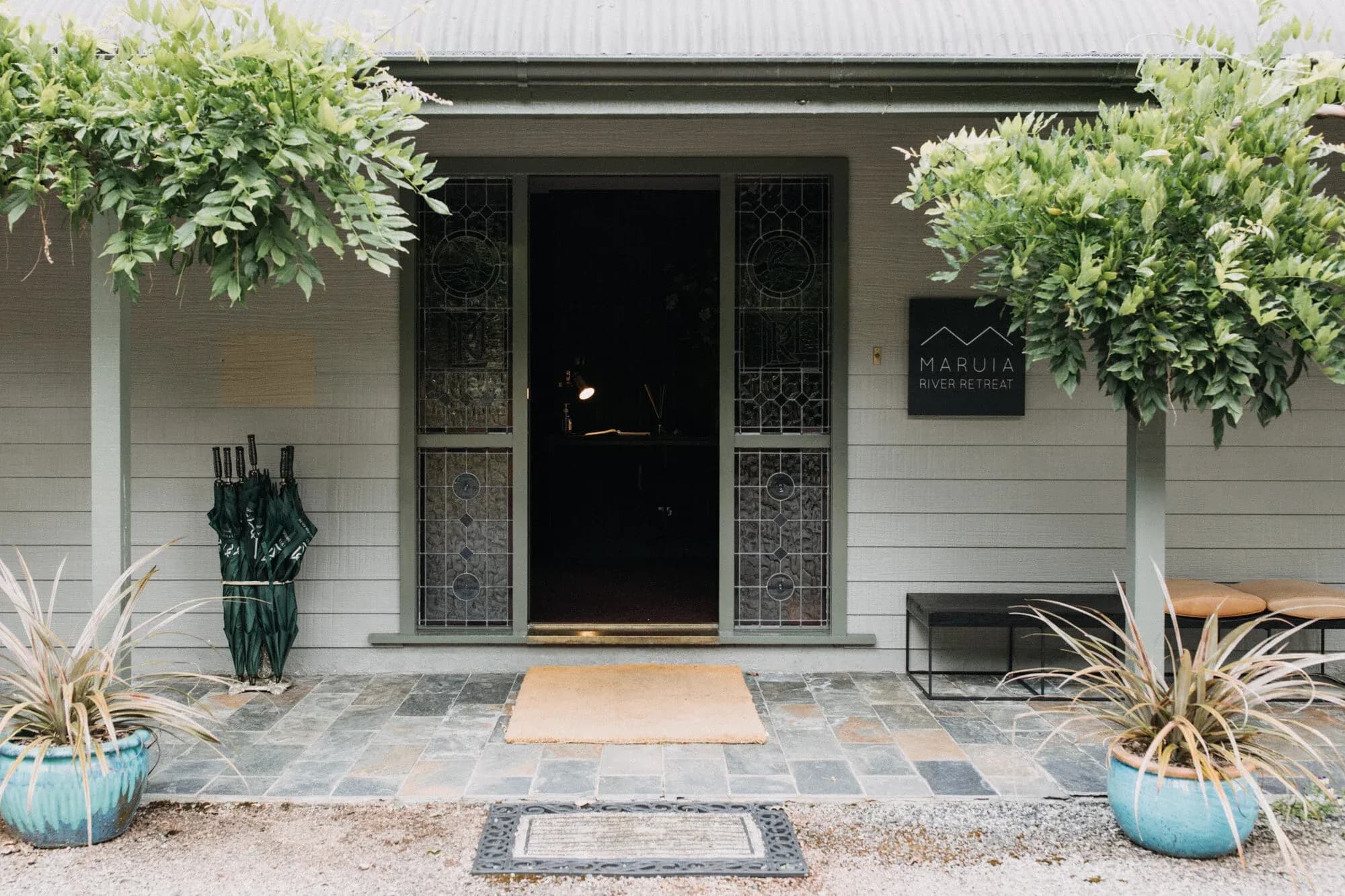 Entrance to Maruia River Retreat featuring a stone pathway, decorative planters, and a wooden door with stained glass panels.