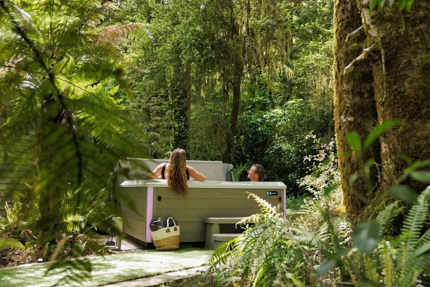 Guests relaxing in a hot tub surrounded by lush greenery and ferns at Maruia River Retreat.