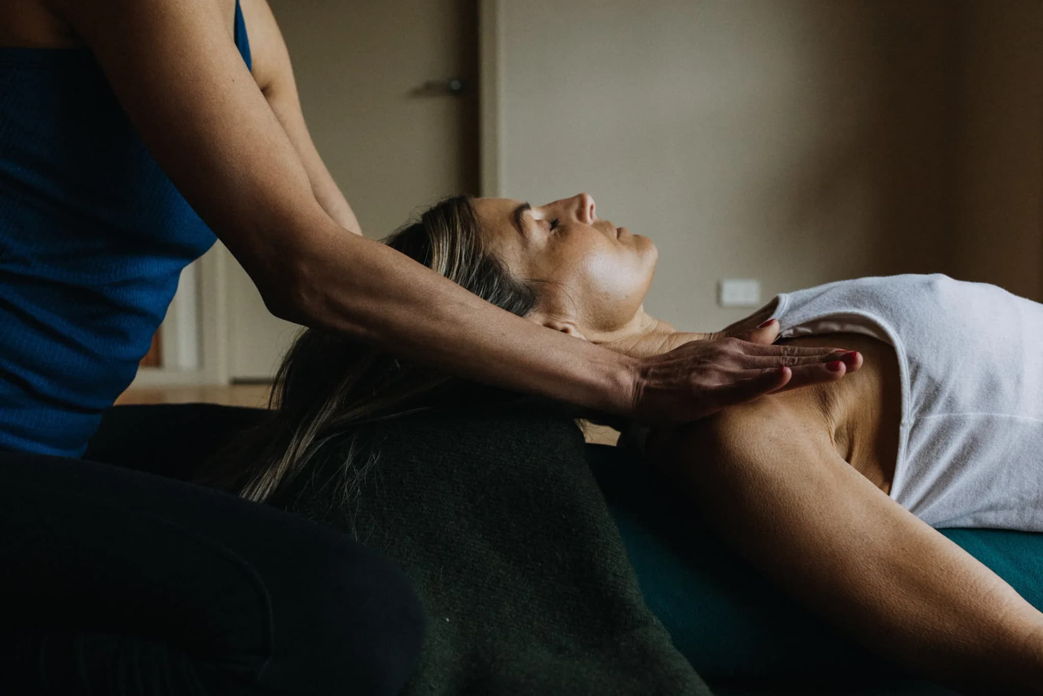 A guest receiving a massage with a therapist's hand on their shoulder, surrounded by neutral-toned walls and soft furnishings.
